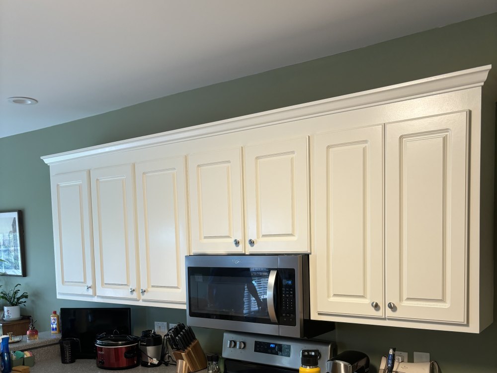 A run of raised-panel wall cabinets finished in cream with crown molding, against a sage-green kitchen wall.