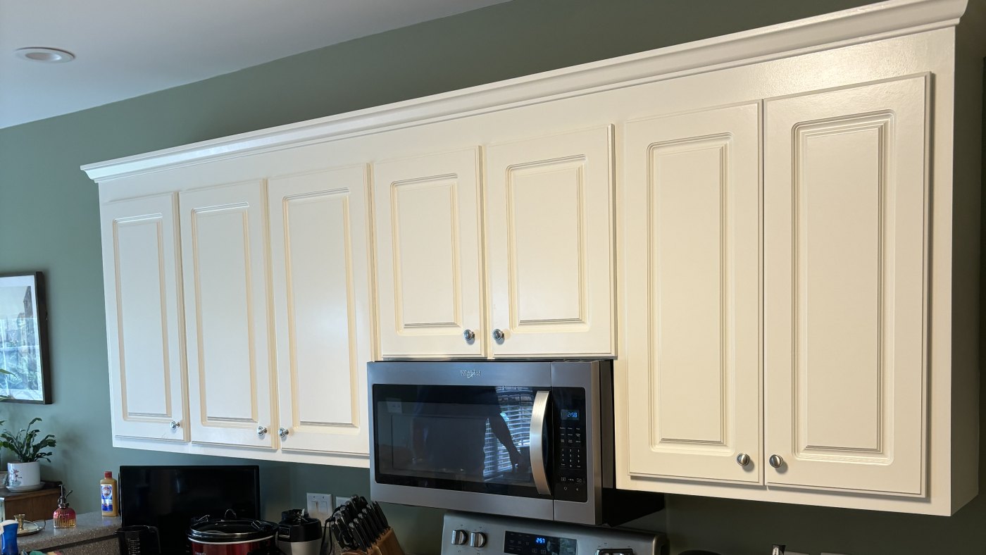 A run of raised-panel wall cabinets finished in cream with crown molding, against a sage-green kitchen wall.