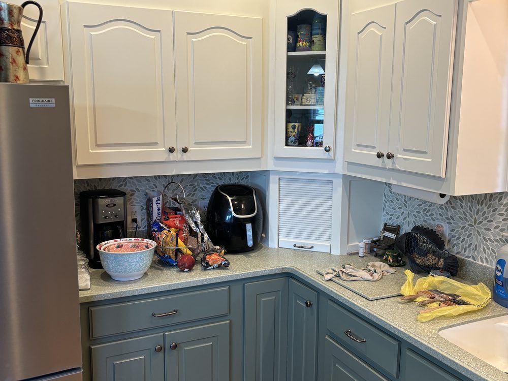 A corner run of kitchen cabinets with white painted uppers and darker painted lower doors and drawers, above a wood floor.