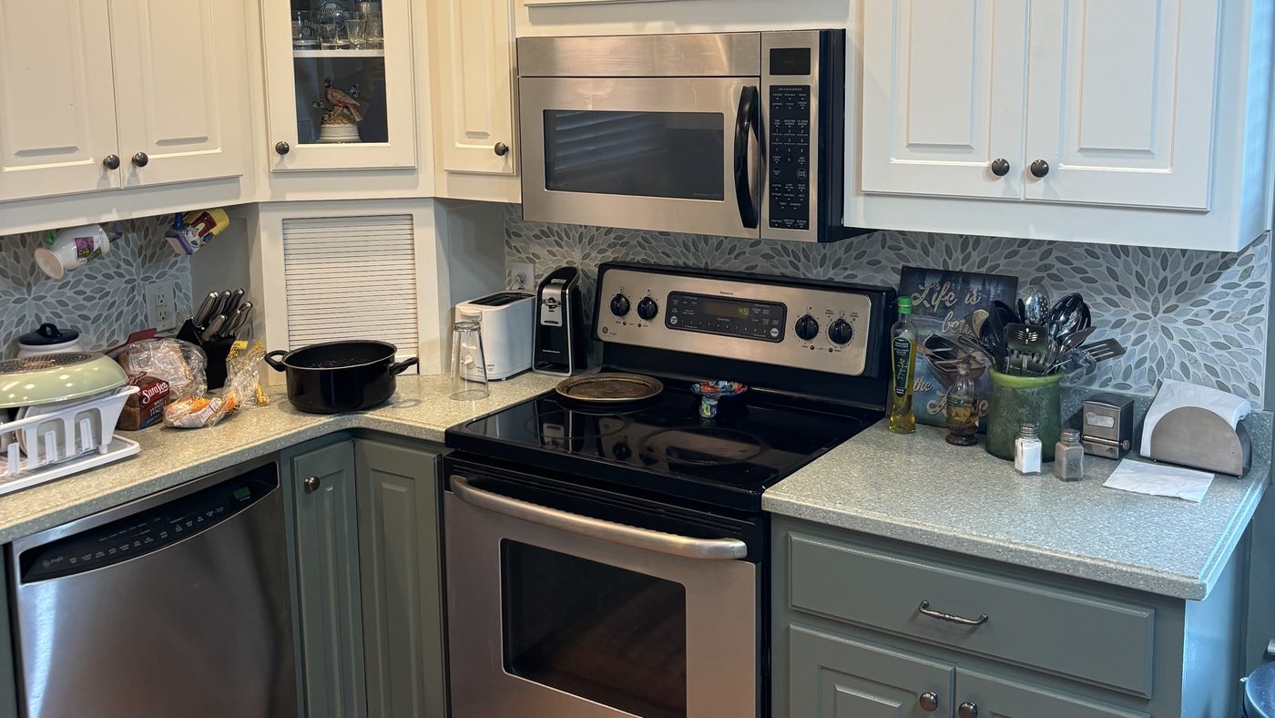 A kitchen with white painted upper cabinets and darker painted lower cabinets, with stainless steel appliances and a patterned tile backsplash.