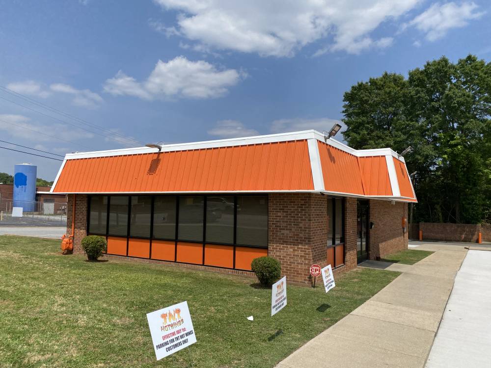 A single-story brick commercial building with an orange standing-seam metal roof and matching orange window panels, seen from the street.
