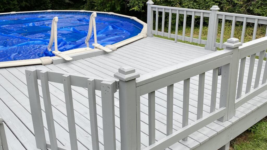 A painted timber pool deck with a white railing and a gate, running alongside an above-ground pool under its cover.