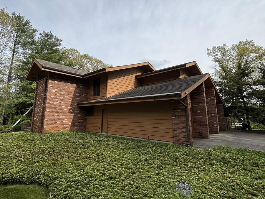 A two-story house with brown wood siding and a brick garage wall, seen from a sloping lawn.