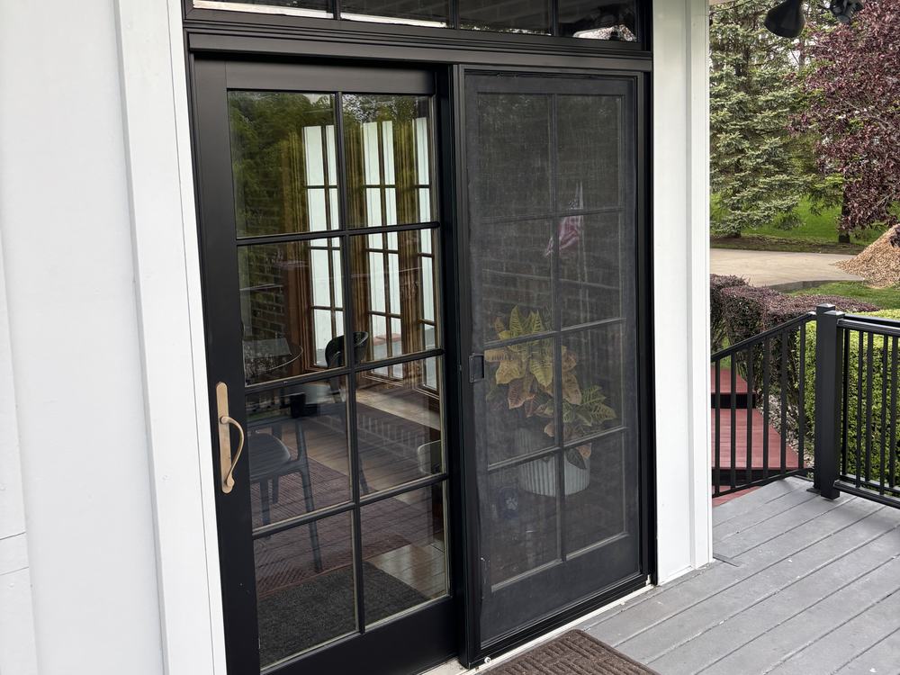 Black glazed doors and a screen door under a covered deck, with a white painted beadboard soffit above and a gray deck floor below.