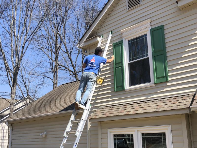 A cream-sided two-story house with an attached garage, dark green shutters at the upstairs windows and a ladder set against the siding.