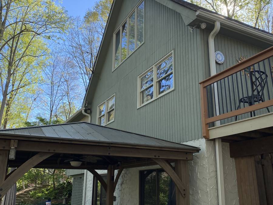 A sage-green board-and-batten gable above a timber porch with a metal roof, with a railed balcony to one side.