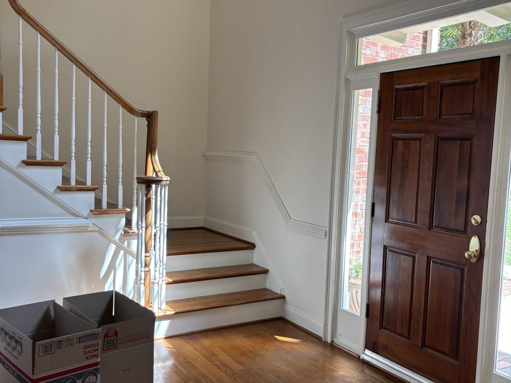 An entry hall with a stained front door, white balusters and a turned newel post, above a hardwood floor.