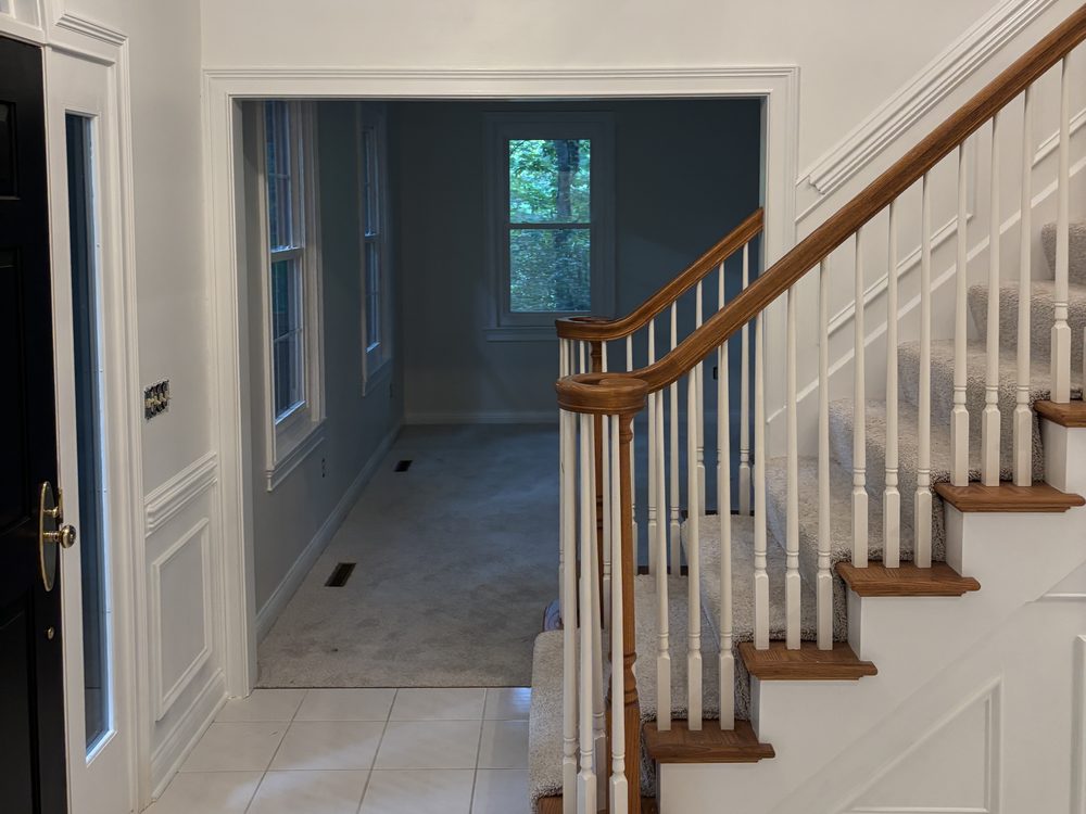 A freshly painted entry hall with white trim, paneled wainscot and a carpeted staircase, opening into a room painted a darker shade.