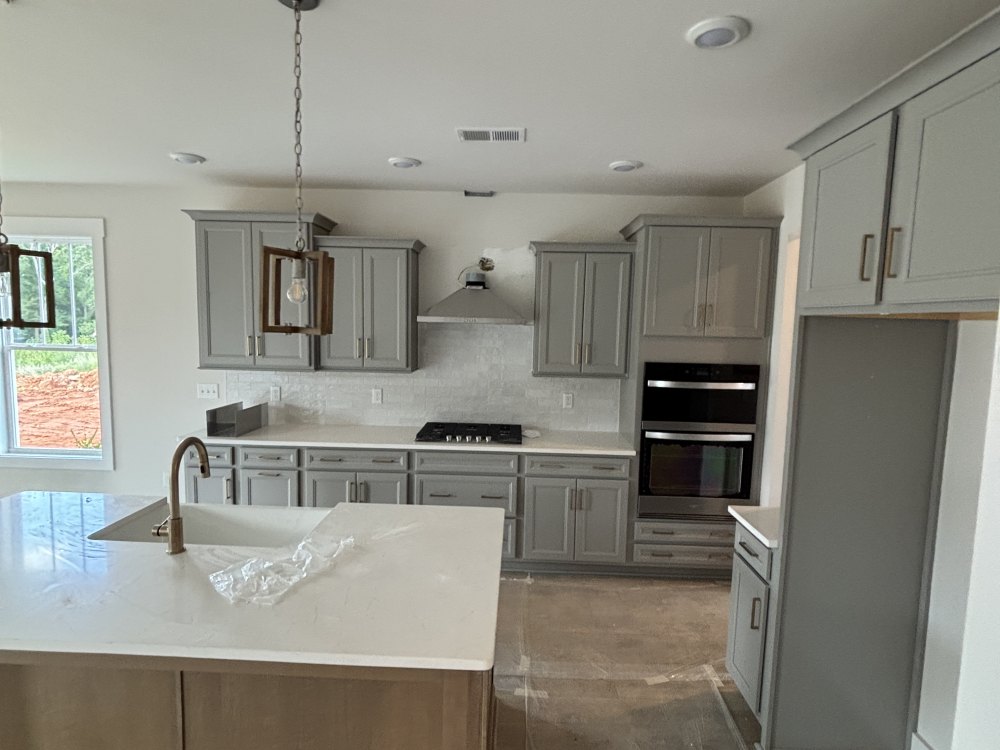 A kitchen with gray painted cabinets, a pale stone worktop and an island, with paper protection still down over the floor.