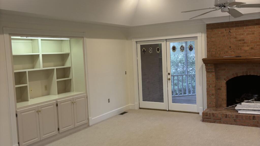 An empty living room with freshly painted walls, white built-in shelving beside glazed doors, and a red brick fireplace.