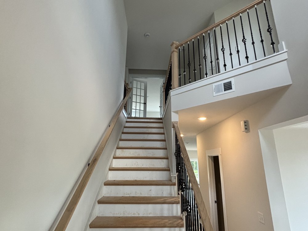 A staircase rising to an open landing in a two-story hall, with painted walls, a wooden handrail and iron balusters.