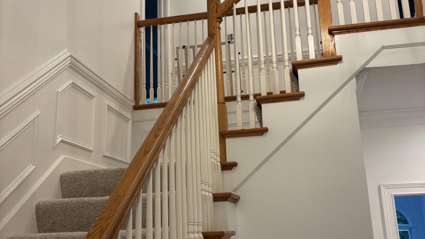An interior staircase with white paneled wainscot, white balusters and a stained oak handrail, lit by a black lantern pendant.