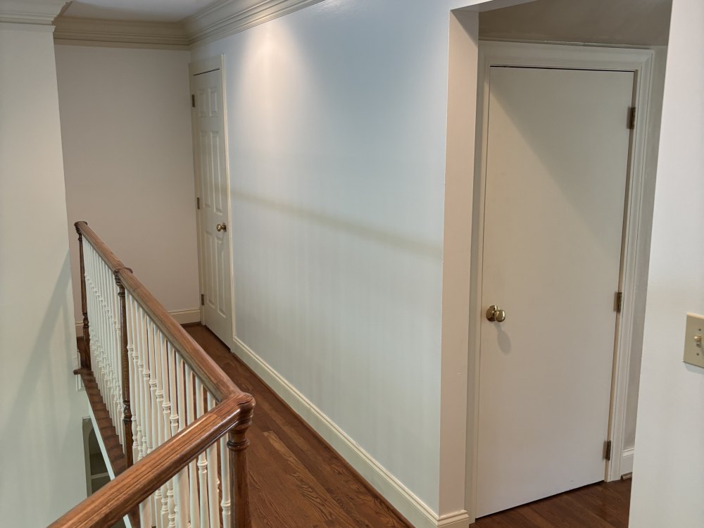 An upstairs landing painted pale blue, with white crown molding, white doors and a stained handrail along the stairwell.